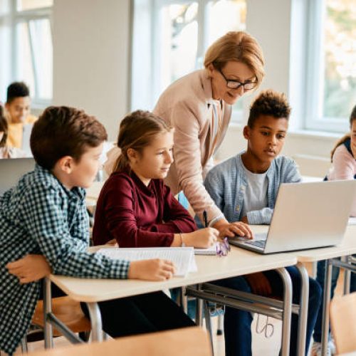Elementary teacher and her students using laptop during computer class at school.